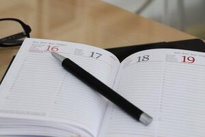 Bild vergr&ouml;&szlig;ern: Ein aufgeschlagener Kalender, ,auf dem ein Stift liegt.