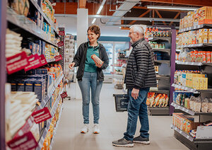 Bild vergr&ouml;&szlig;ern: Ein Mann steht vor einem hohen Warenregal in einem Supermarkt und wird von einer Verkäuferin beraten.