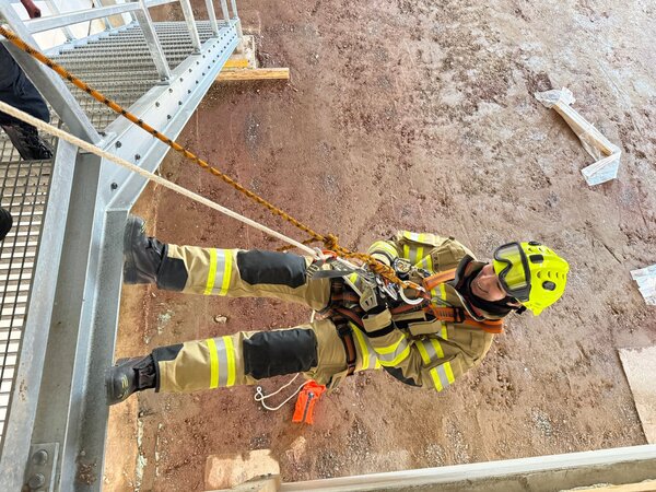 Bild vergr&ouml;&szlig;ern: Eine Feuerwehrfrau in Uniform seilt sich von einem Treppenabsatz aus mehreren Metern Höhe ab.