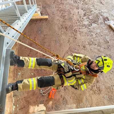 Eine Feuerwehrfrau in Uniform seilt sich von einem Treppenabsatz aus mehreren Metern Höhe ab.