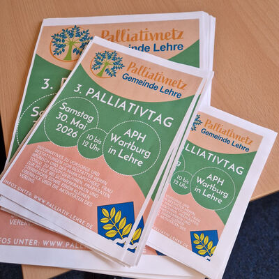 Plakate zum Palliativtag in mehreren Größen líegen gestapelt auf einem Tisch.