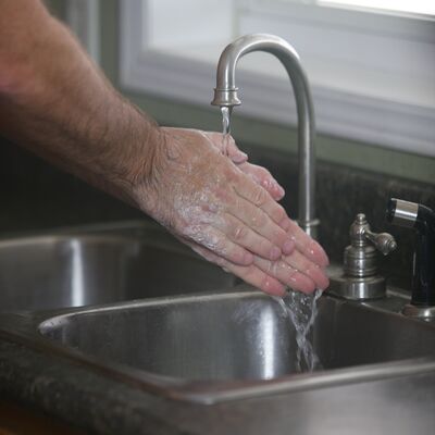 Eine männliche Person wäscht sich die Hände unter einem Wasserhahn.