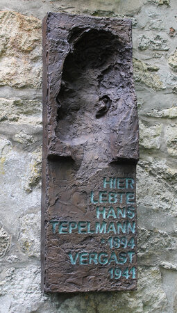Bild vergr&ouml;&szlig;ern: Das Bronzerelief des Künstlers Denis Stuart Rose zeigt das Konterfei von HansTepelmann als Negativform. Darunter ist die Inschrift "Hier lebte Hans Tepelmann *1894 vergast 1941, zu lesen.