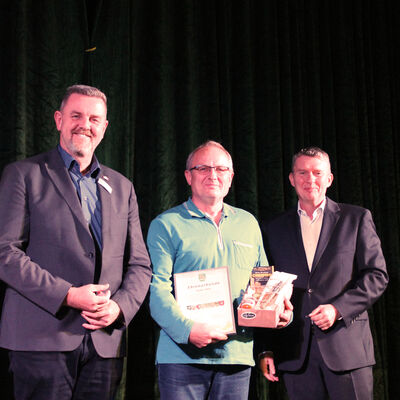 Gemeindebürgermeister Andreas Busch(links) und Ortsbürgermeister Robert Steinborn(rechts) gratulieren Peter Ebel zu seiner Ehrung. Der Geehrte in der Mitte hält eine Urkunde und eine Präsentbox in den Armen.