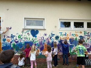 Bild vergr&ouml;&szlig;ern: Viele Kinder malen mit Finderfarbe auf der Hasuwand des alten Kitagebäudes, da bereits kunterbunt gefärbt ist.
