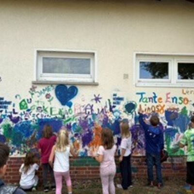 Viele Kinder malen mit Finderfarbe auf der Hasuwand des alten Kitagebäudes, da bereits kunterbunt gefärbt ist.