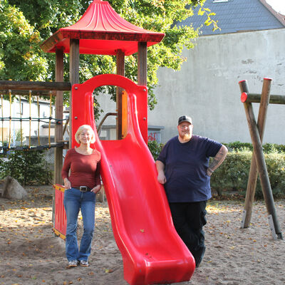 Auf dem Spielplatz setehn links und rechts neben einer roten Rutsche links Nicole Klostermann und rechts Heiko Hülsebus.