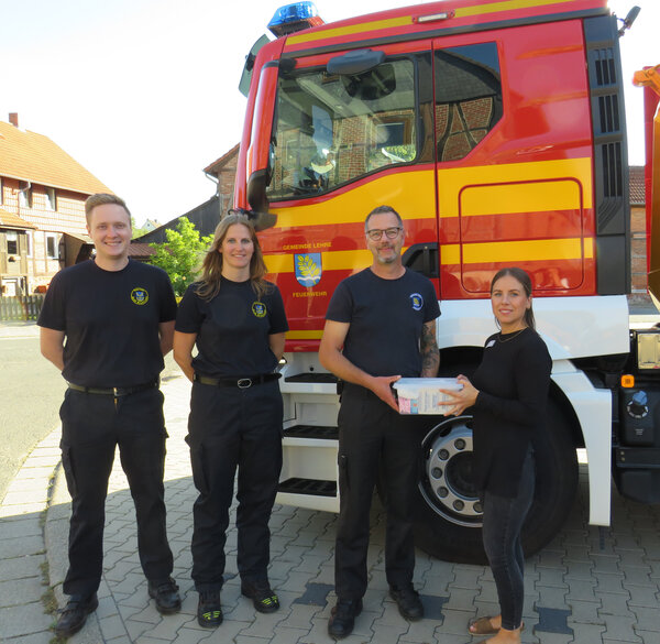 Bild vergr&ouml;&szlig;ern: Vier Personen stehetn vor dem Führerhaus eines Feuerwehrfahzeuges. Frau WEstpahl übergibt Herrn Görke eine kleine befüllte durchsichtige Plastikbox.