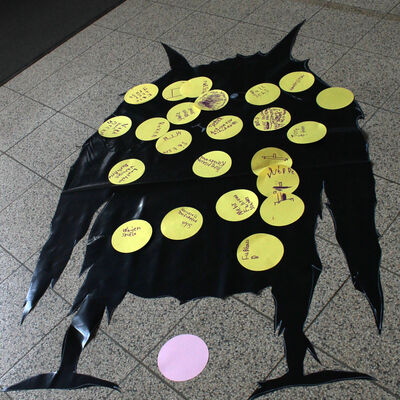 Bild vergr&ouml;&szlig;ern: ,Auf dem Boden liegt der Umriss eines schwarzen "Motzmonsters". Darauf sind farbige "Motzpickel" verteilt. Auf die bunten Papierpunkte haben die Kinder geschrieben und gemalt, was Ihnen am jetzigen Spielplatz nicht gefällt.