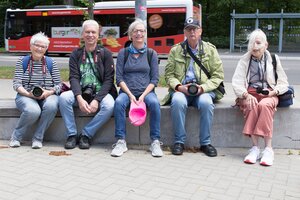 Bild vergr&ouml;&szlig;ern: Fünf Personen sitzen nebeneinander auf einer niedrigen Mauer. Sie sind mit Fotokameras ausgerüstet.