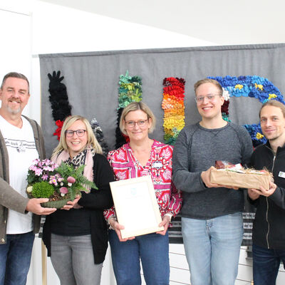 Die Jubilarin steht in der Mitte und hält eine gerahmte Urkunde in den Händen. Links davon stehen Bürgermeister Andreas Busch und Fachbereichsleitung Vanessa Rothermund, die eine bepflanzte Schale überreichen. Rechts neben ihr stehen ihr Kollege Tim Frickmann und Personalratsmitglied Chris Schulze, die ein kleines Präsent übergeben.